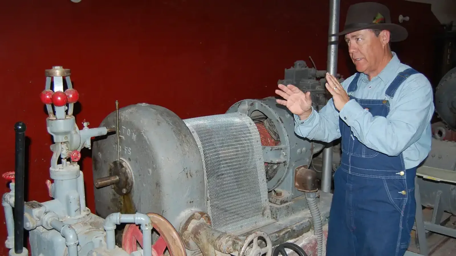 A park ranger dressed as a worker in the 1930s stands talking next to the Pelton water wheel.