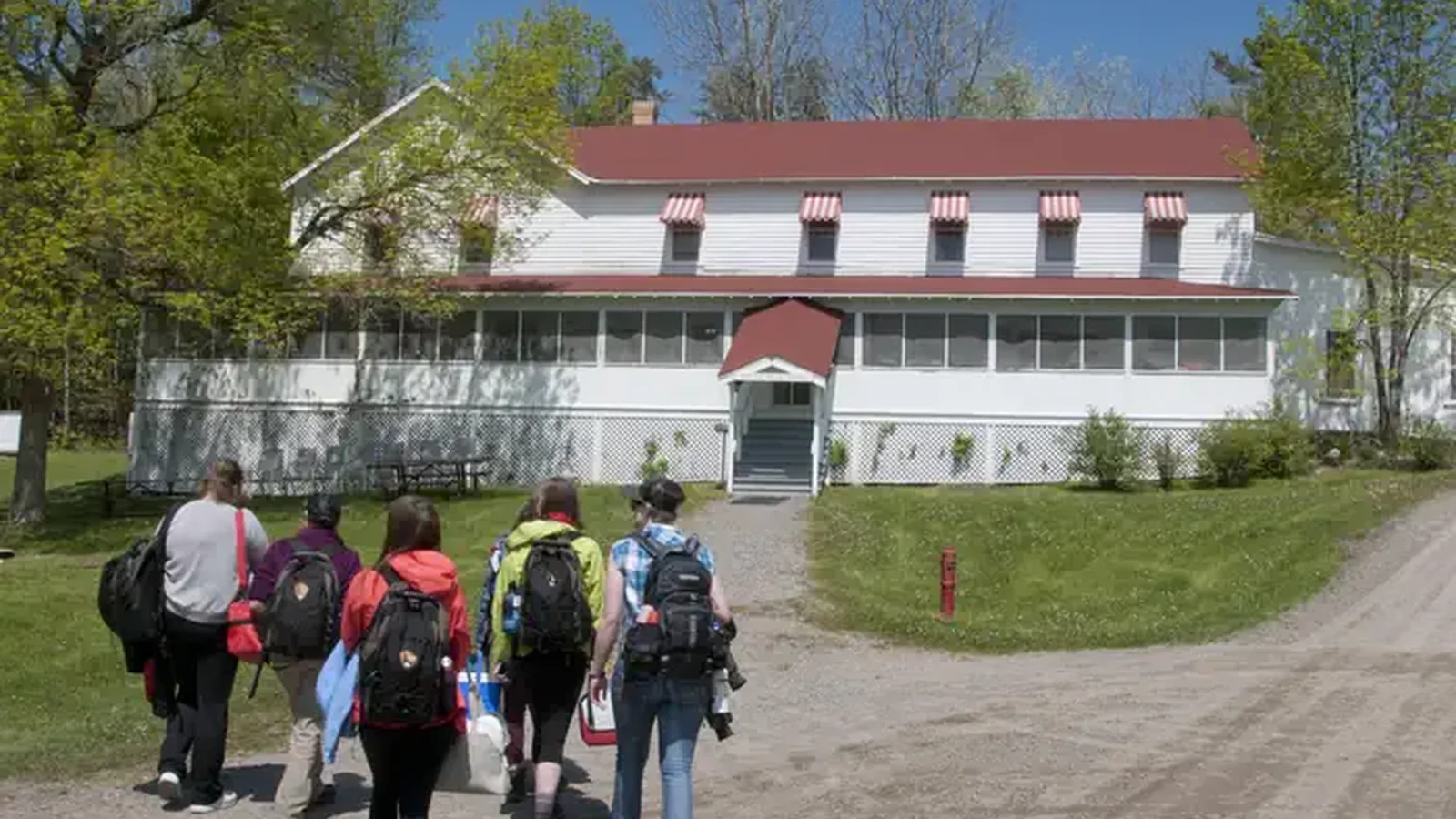 Five people are seen walking towards the painted white clapboard and red awnings of the Kettle Falls Hotel.