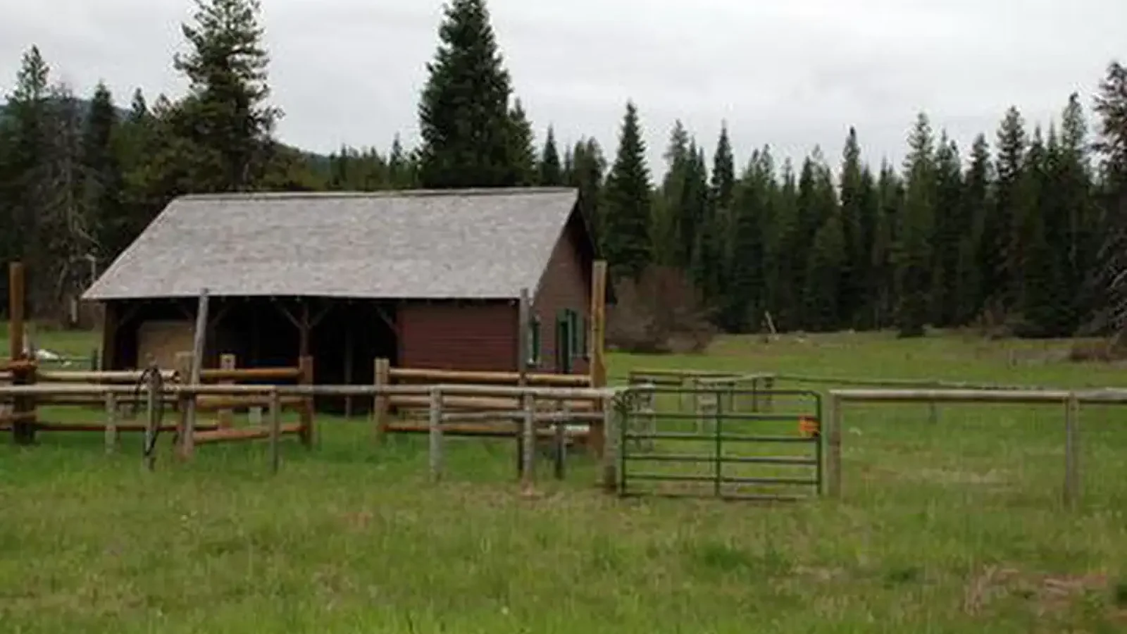 Cabin with red siding and fences in flat meadow backed by conifer forest