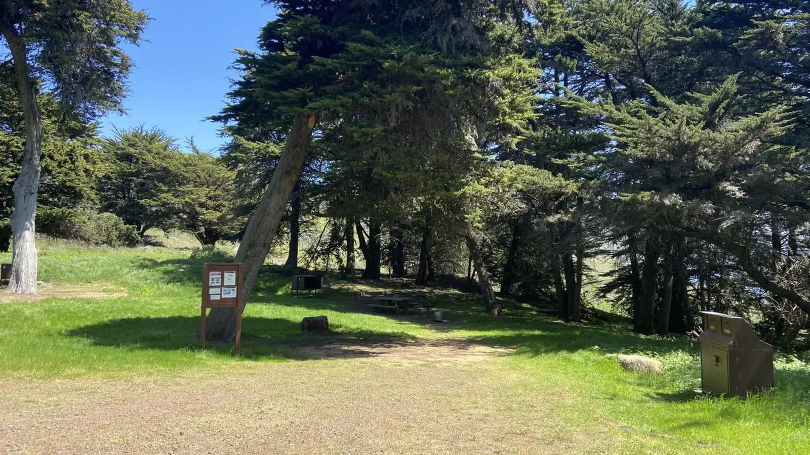Campground with sign post, trashcans, and three campsites splayed across a meadow.