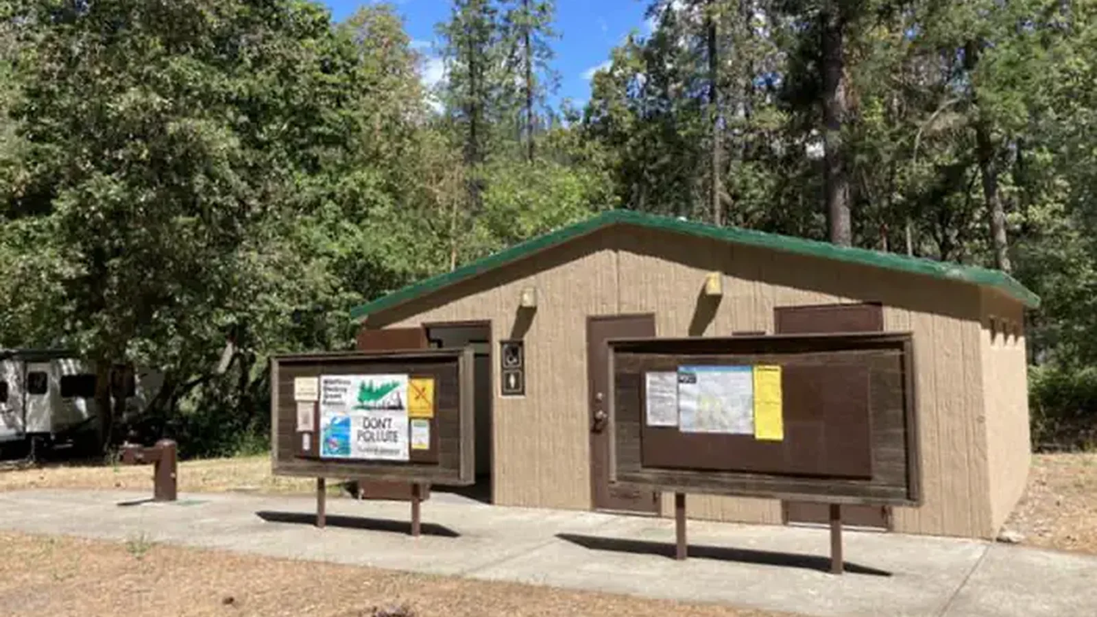 Tan building with green room and brown notice boards in front.