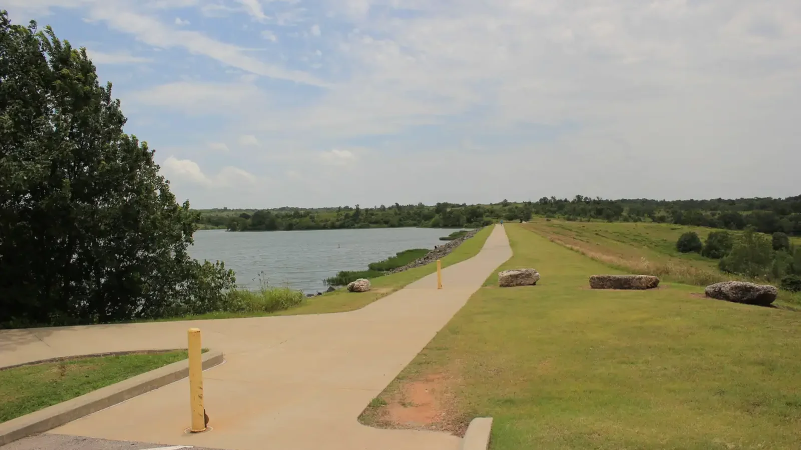 A view of the dam area and trail on Veteran's Lake under a blue sky with cirrus clouds