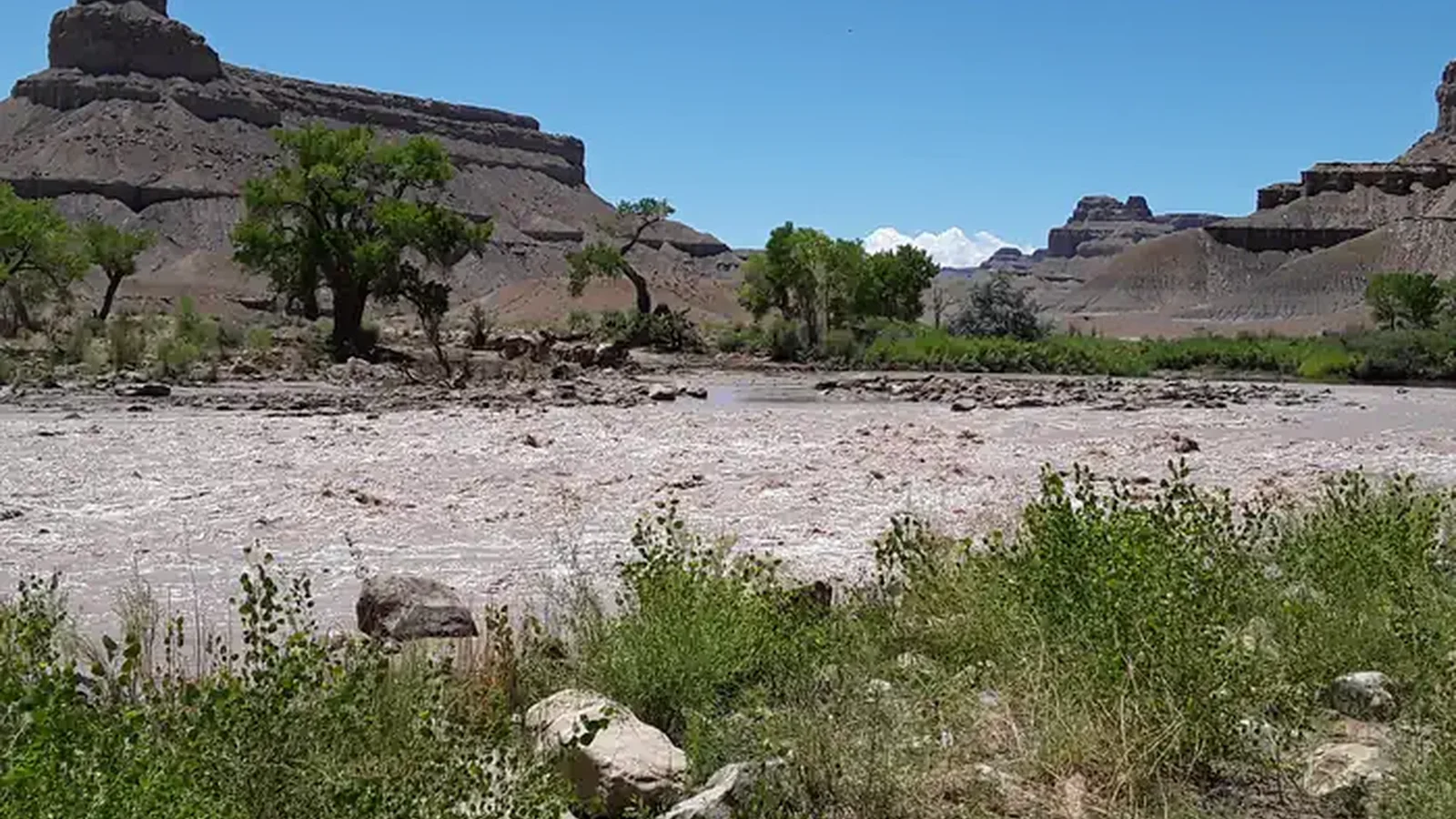 A photo looking across a river rapid to low buttes on the other side