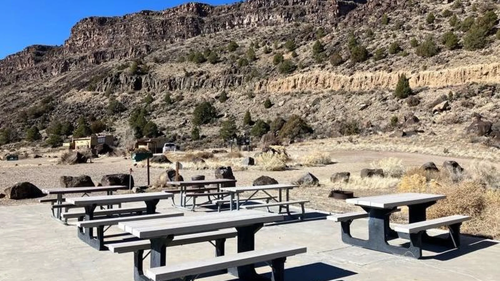 A view of the Taos Junction group site area with picnic tables, concrete pad, fire pan, and trash receptacles.