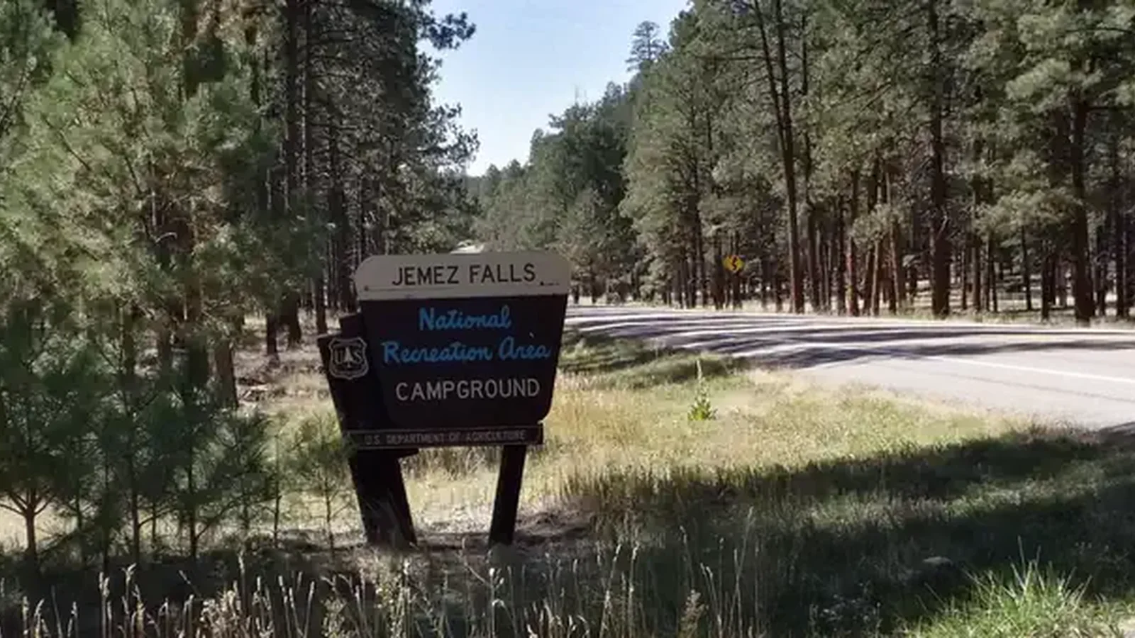 The entrance to Jemez Falls sign with pine forests in the background.