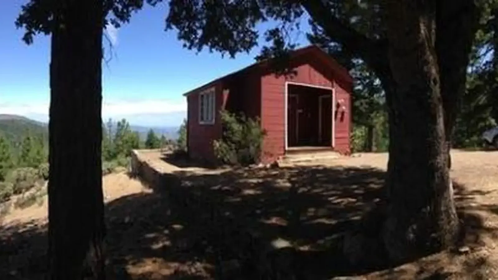 Red cabin in between trees with blue sky in background.