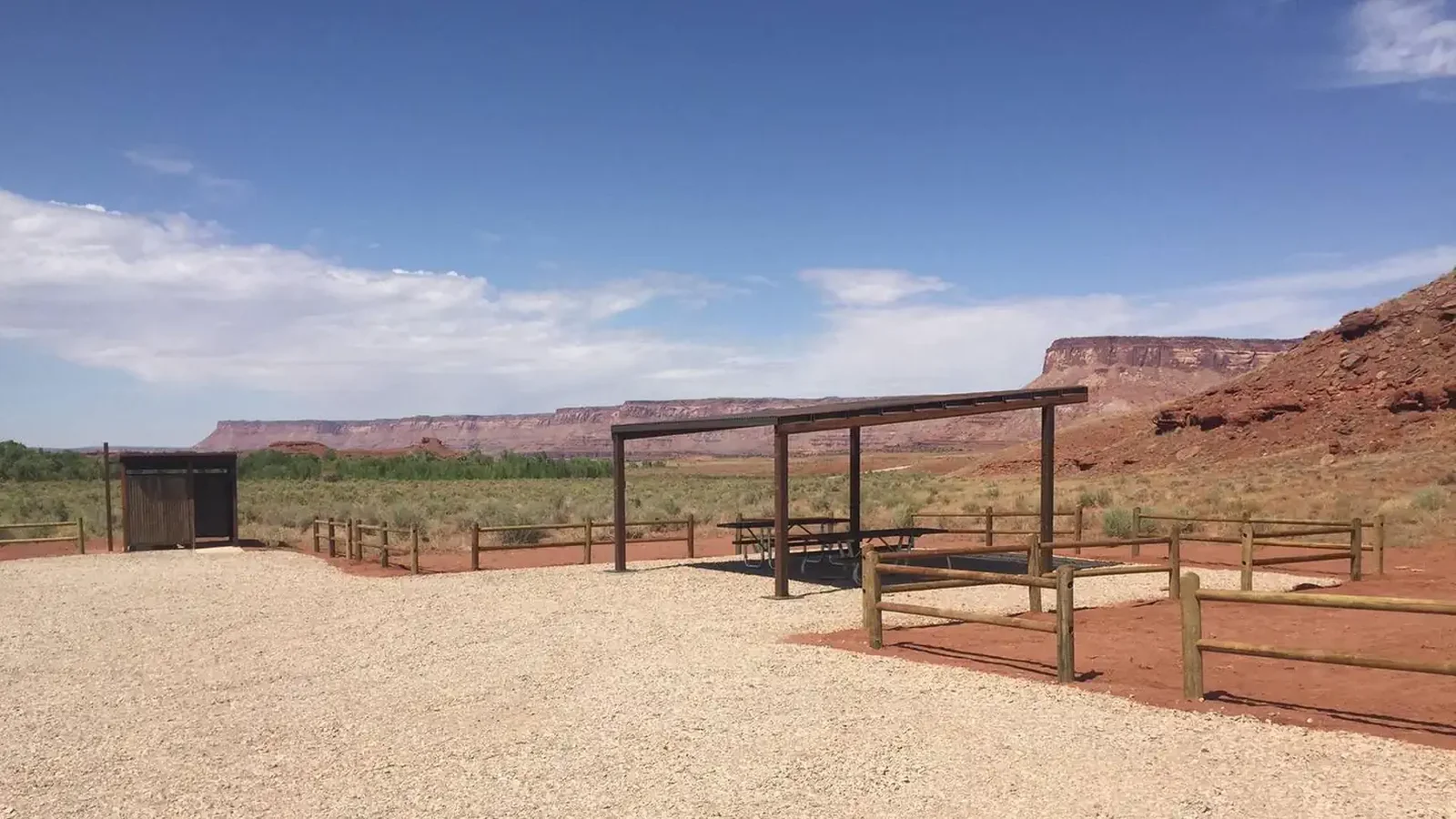 Superbowl group site shad structure and vault toilet with scenic red sandstone cliffs in background.