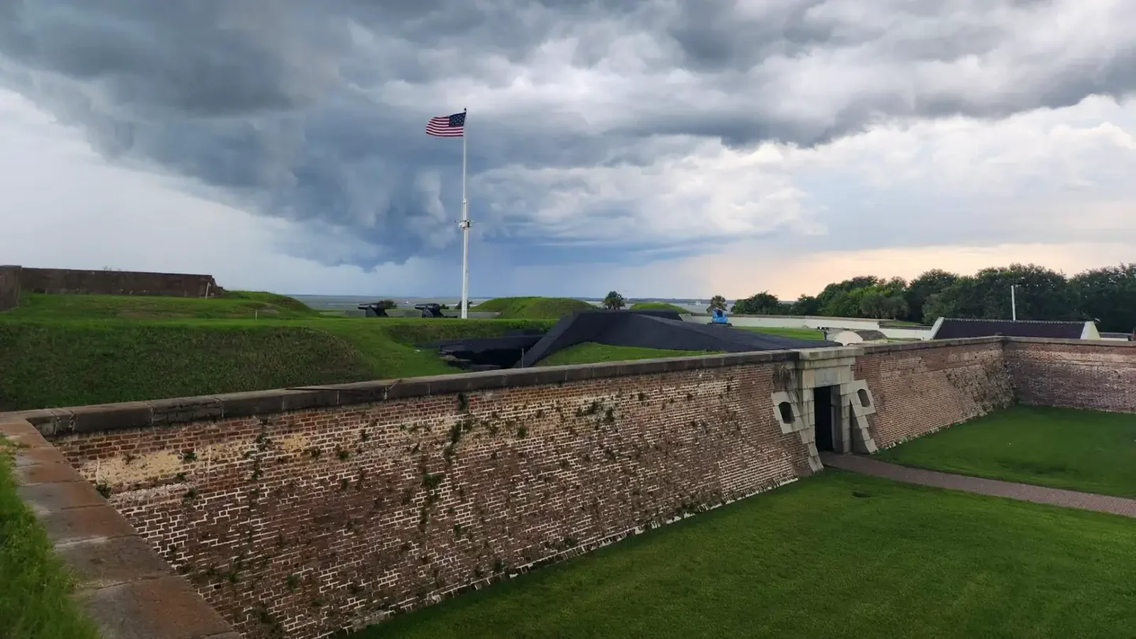Front angle view of Fort Moultrie with storm clouds rolling in overhead and American flag rising up from the fort's interior.