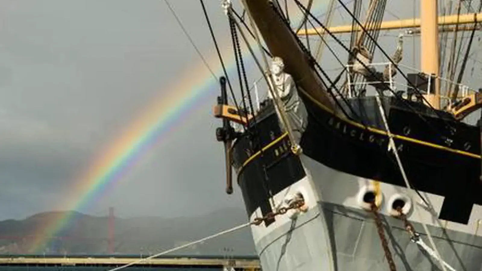 Historic Balclutha's figurehead with a rainbow and Golden Gate Bridge in background.