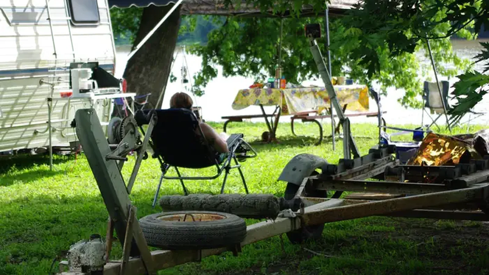 Camper looking out over the river from lawn chair and trailer