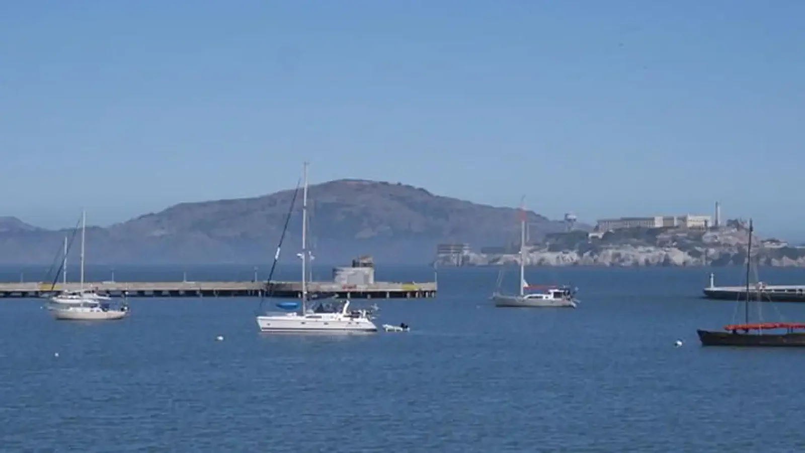 Sailing vessels anchored in Aquatic Park Cove. A view to the northeast under dramatic cirrus clouds with Alcatraz Island in background.