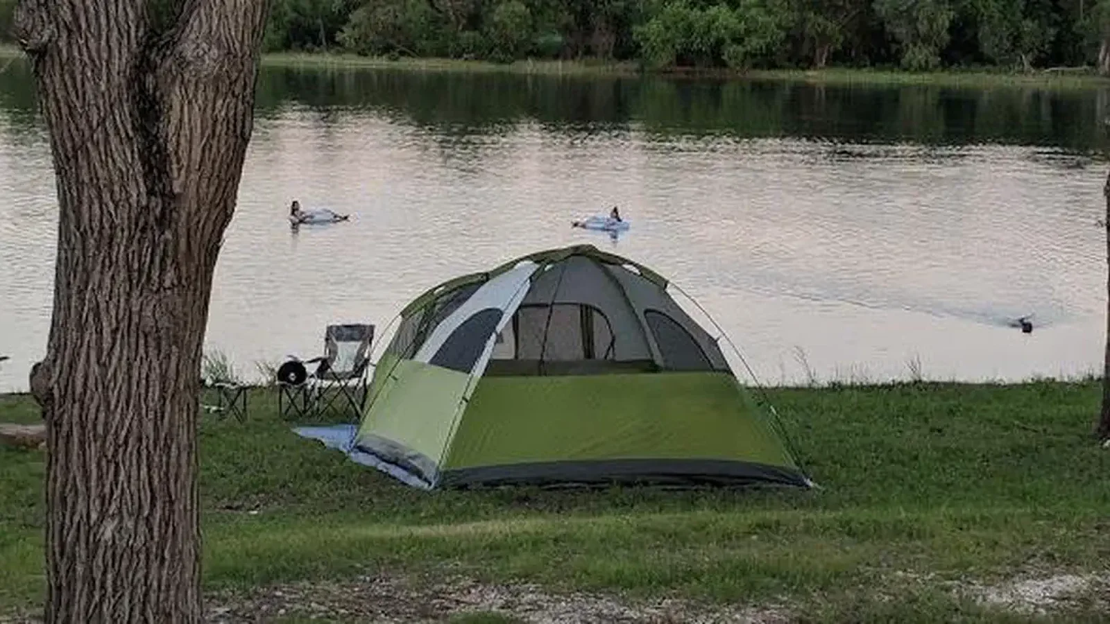 Green tent pitched on the shore of a lake.
