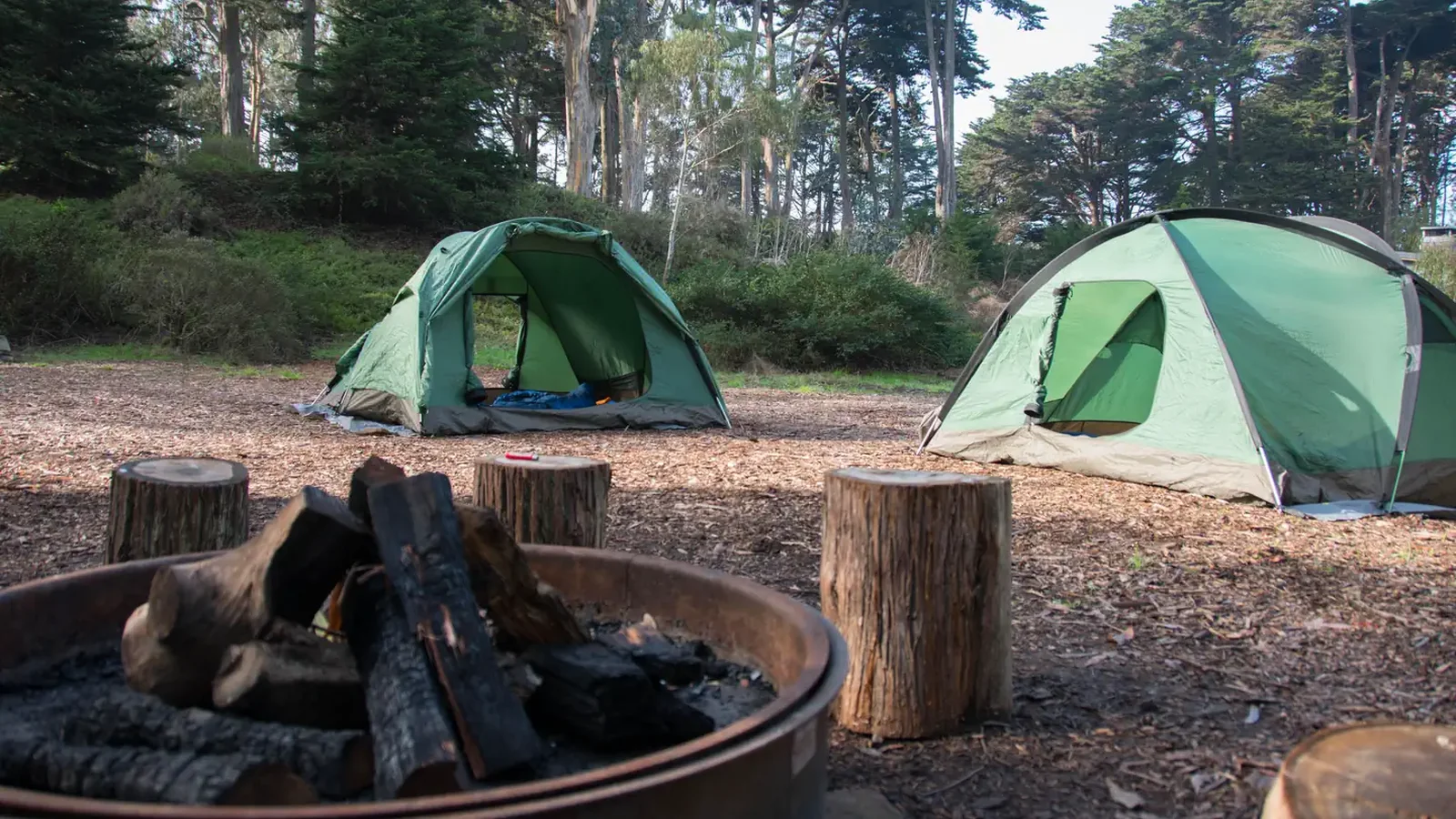 Campsite with metal fire ring in the foreground and two green tents in the background.