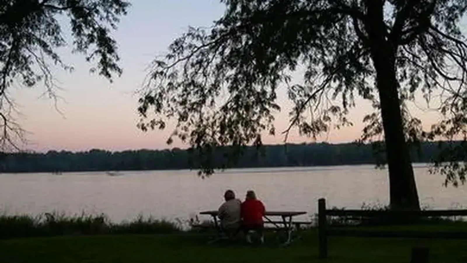 People at a picnic table at sunset overlooking the river.