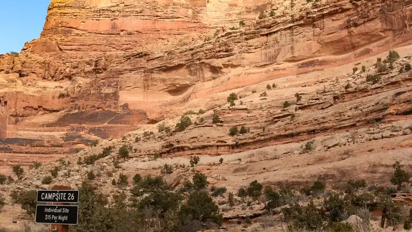 A dirt road with a sign for Campsite 26 leads towards the base of an orange sandstone cliff