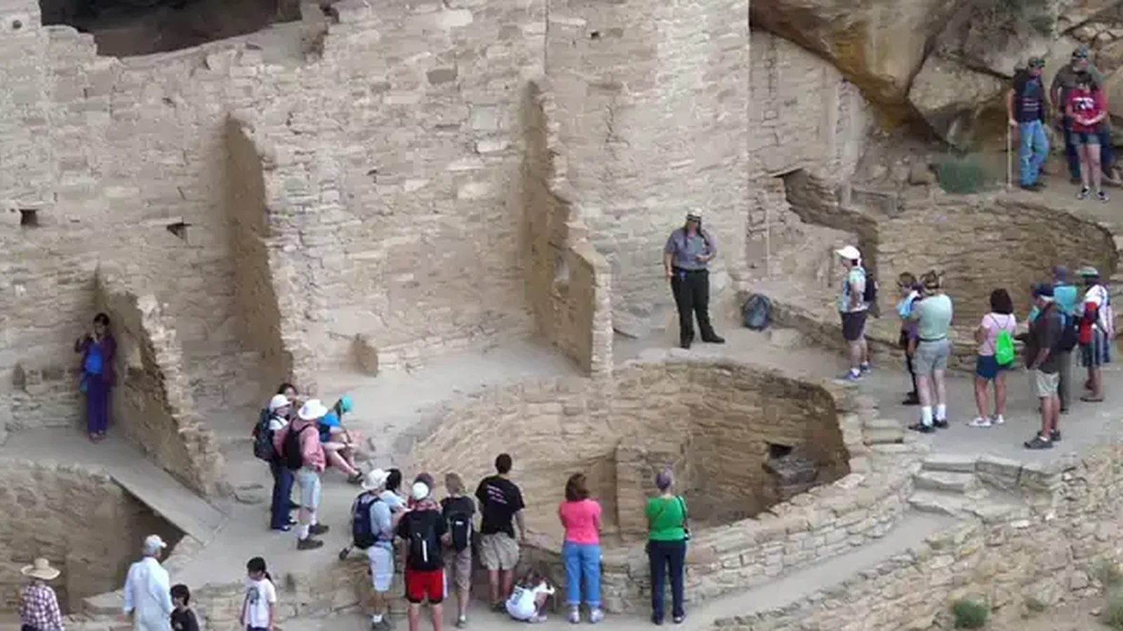 People cluster around three round underground rooms in front of stone buildings.