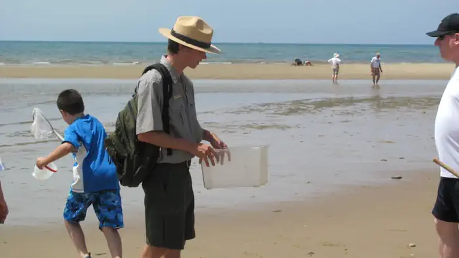 A young boy runs out onto tidal flats behind a ranger looking for beach life.
