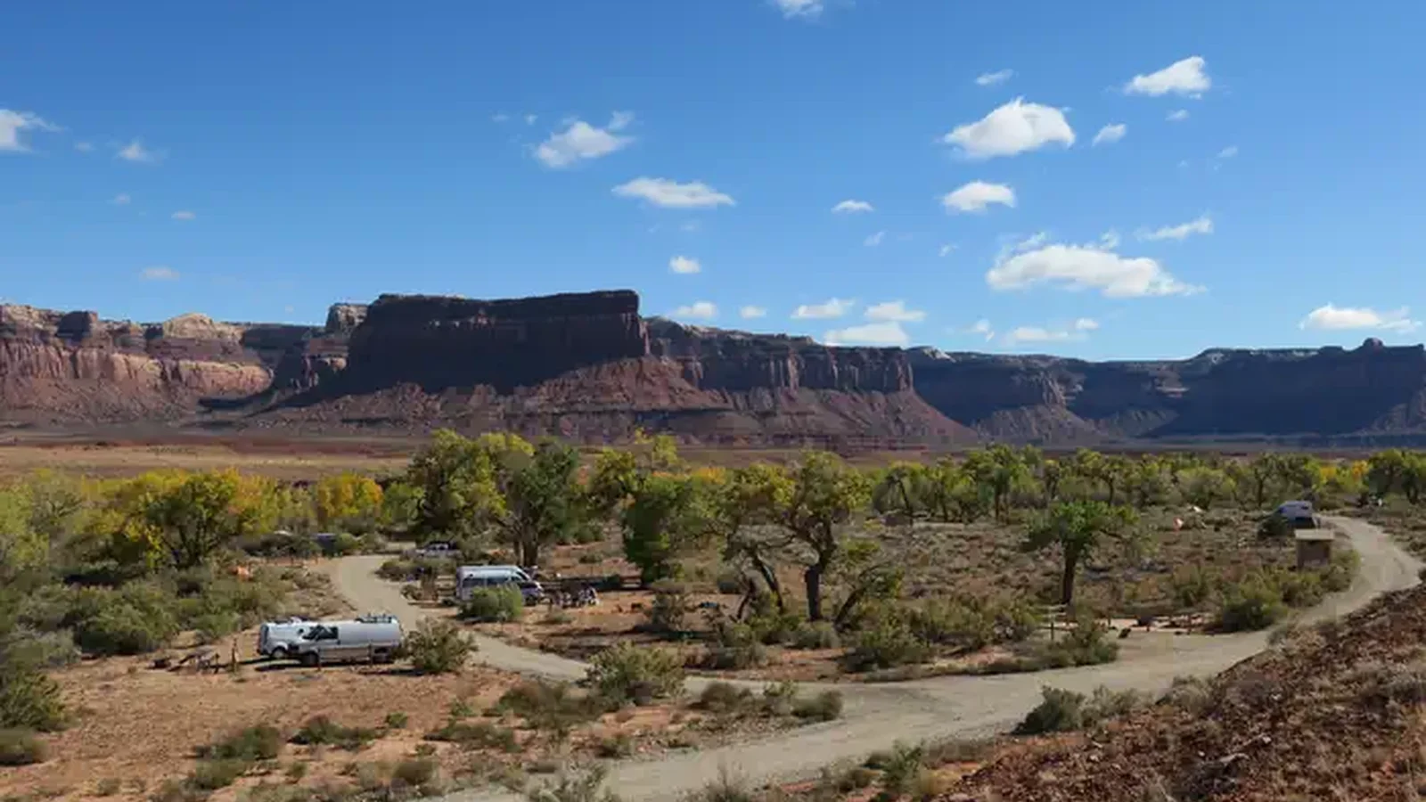 A gravel campground loop road surrounded by Cottonwood trees with red sandstone cliffs in background.