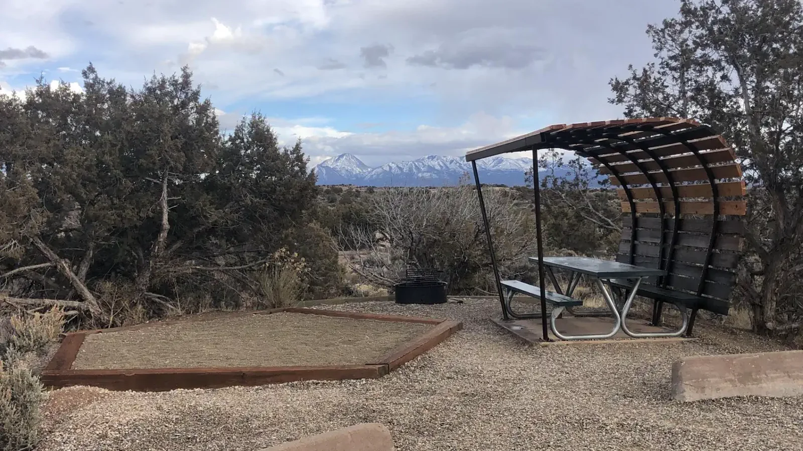 A tent pad and covered picnic table with a background of Sleeping Ute mountain range's snow-covered peaks.