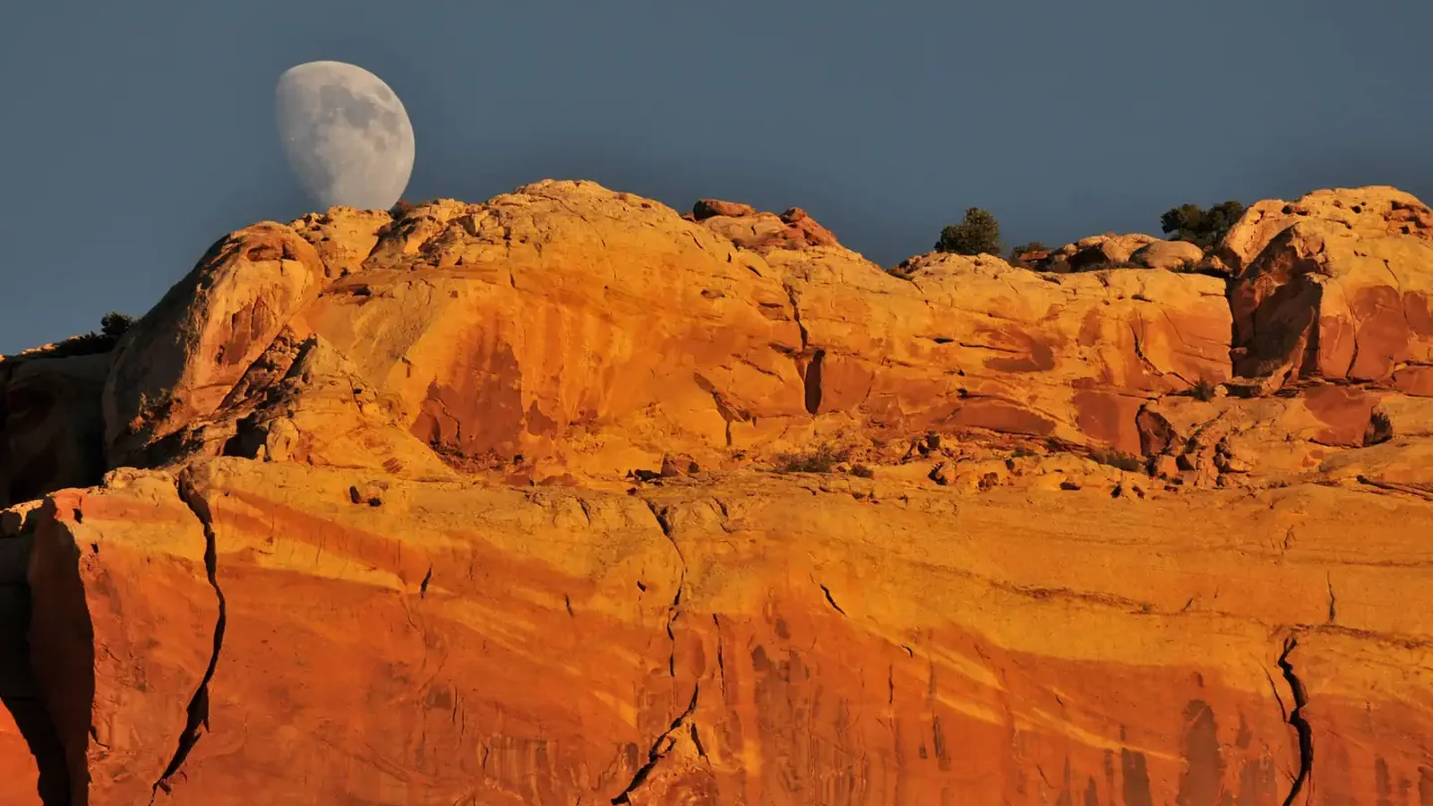 An almost full moon comes over a orange-red colored rock formation.