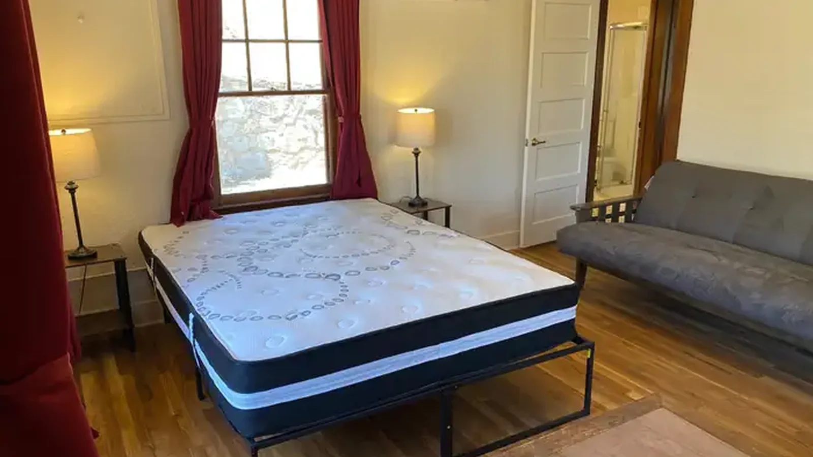 Queen size mattress on bedframe and futon with climate control unit mounted on the wall.