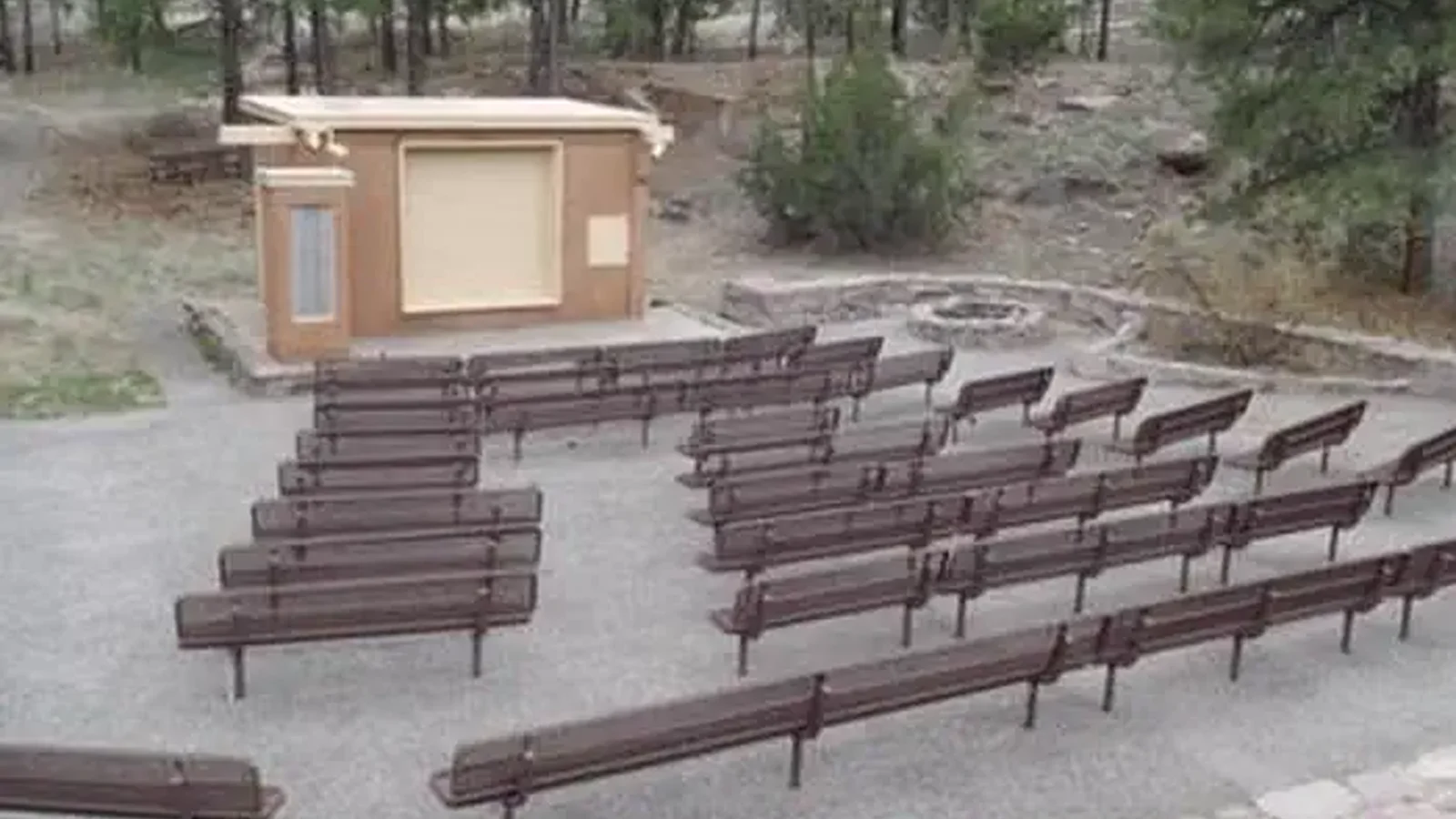 Amphitheater with brown benches and a tan building surrounded by pine trees