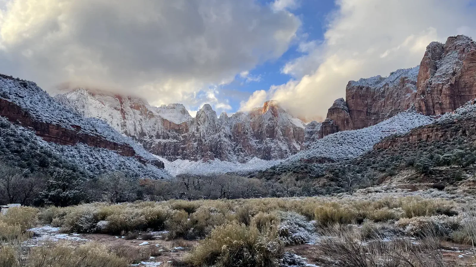 Sandstone peaks covered in snow and shrouded in clouds illuminated by late afternoon sun.