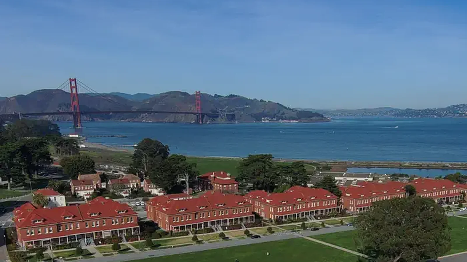 Red brick barrack buildings with lawn in front and the Golden Gate Bridge in the background.