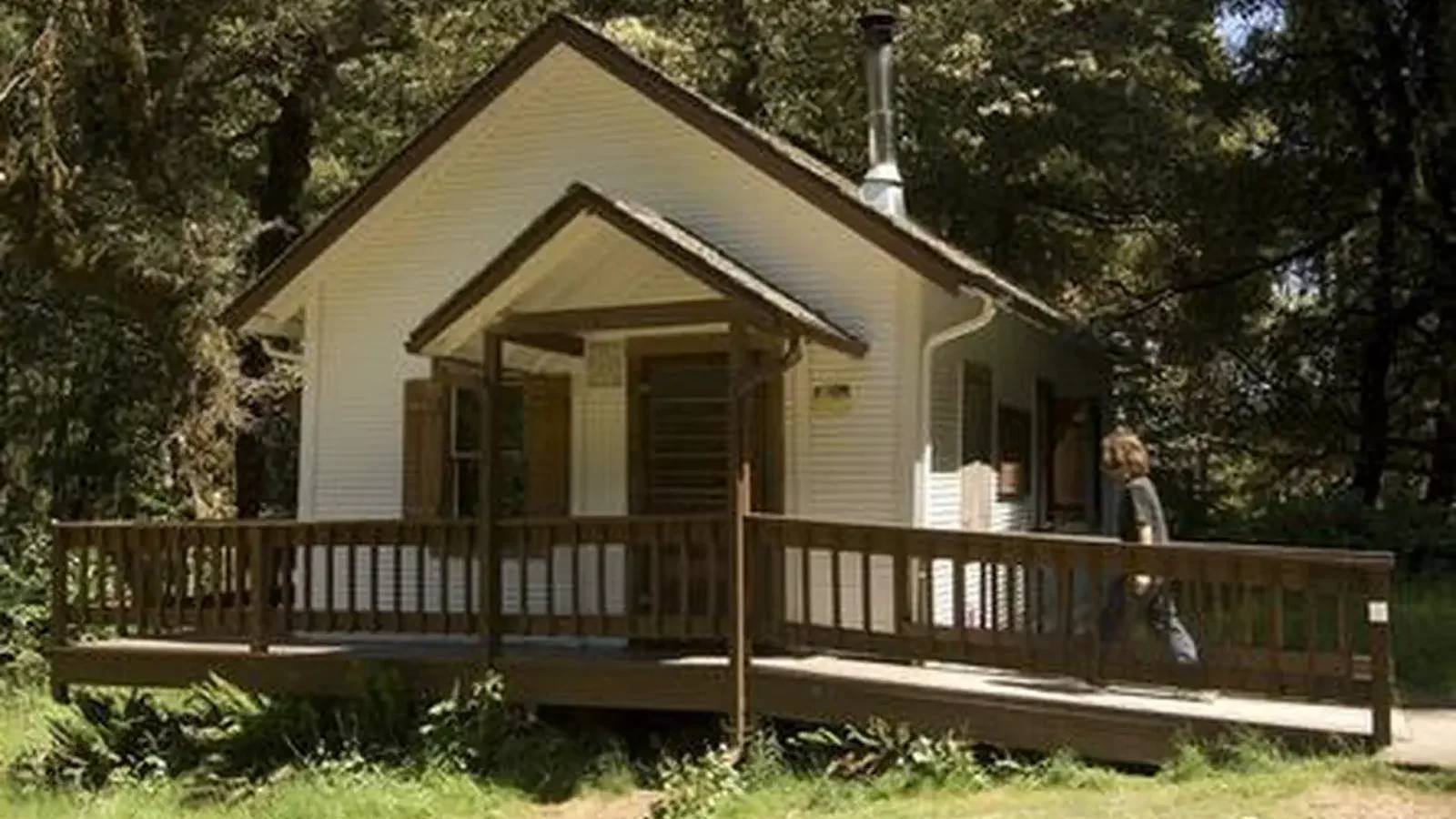 White cabin in the woods with ramp leading to front door and small porch