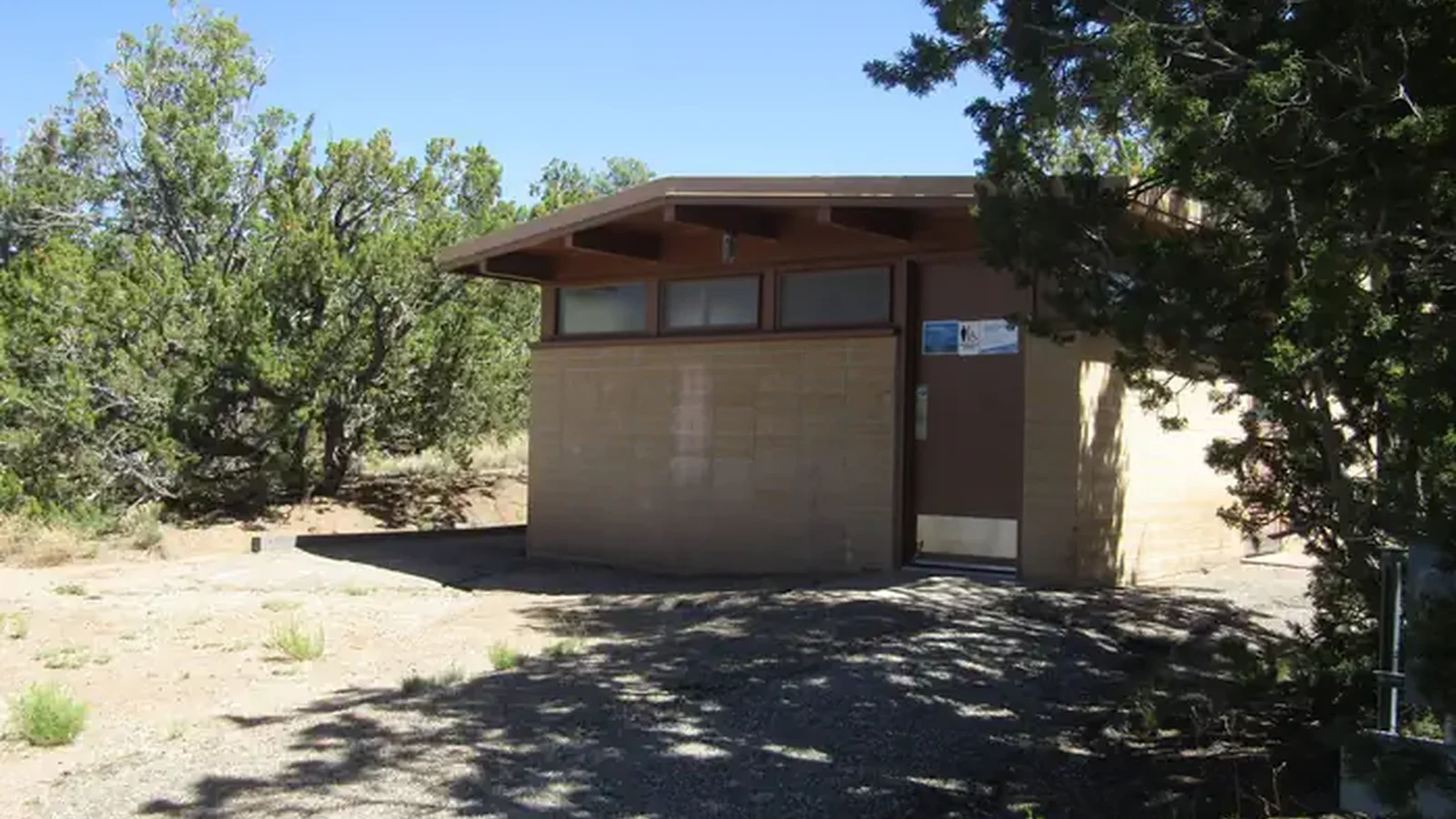 A tan brick building surrounded by juniper.