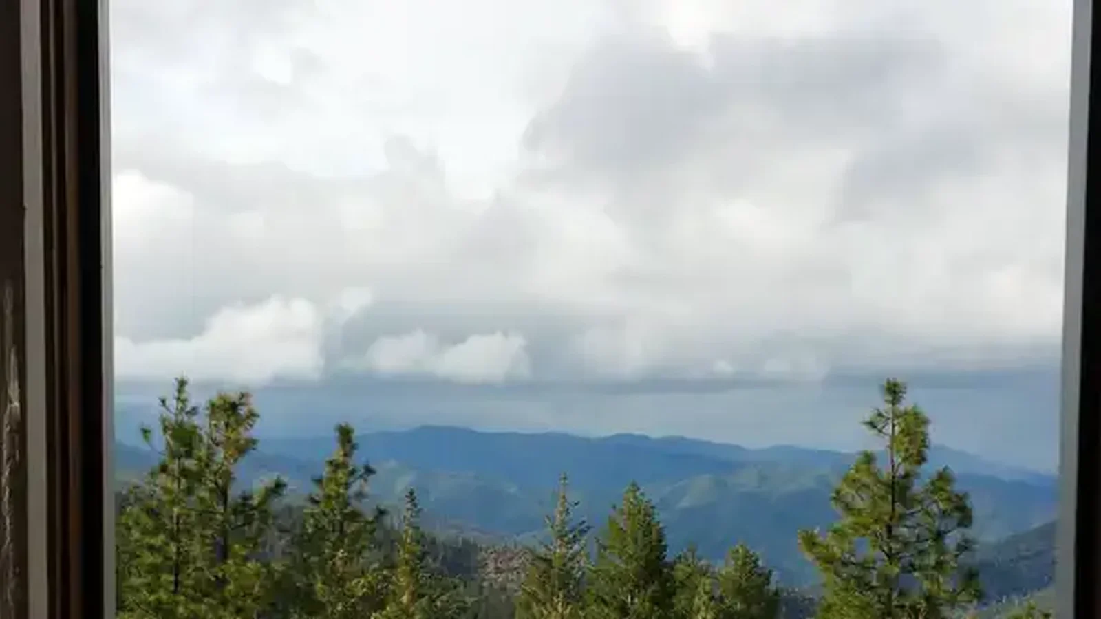 View of mountains and cloudy sky through cabin window.