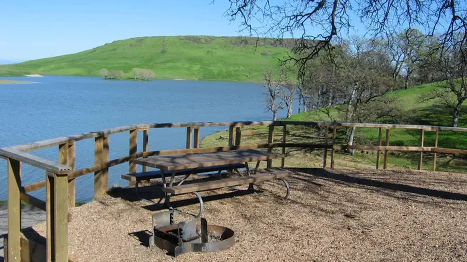 Campsite within Buckhorn Campground showing picnic table, firepit, and lake in background.
