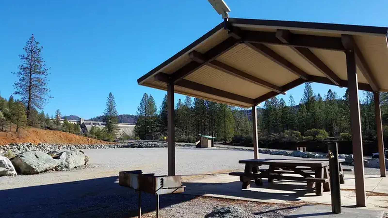 Shade structure, picnic tables, and grills with open camping area in the background