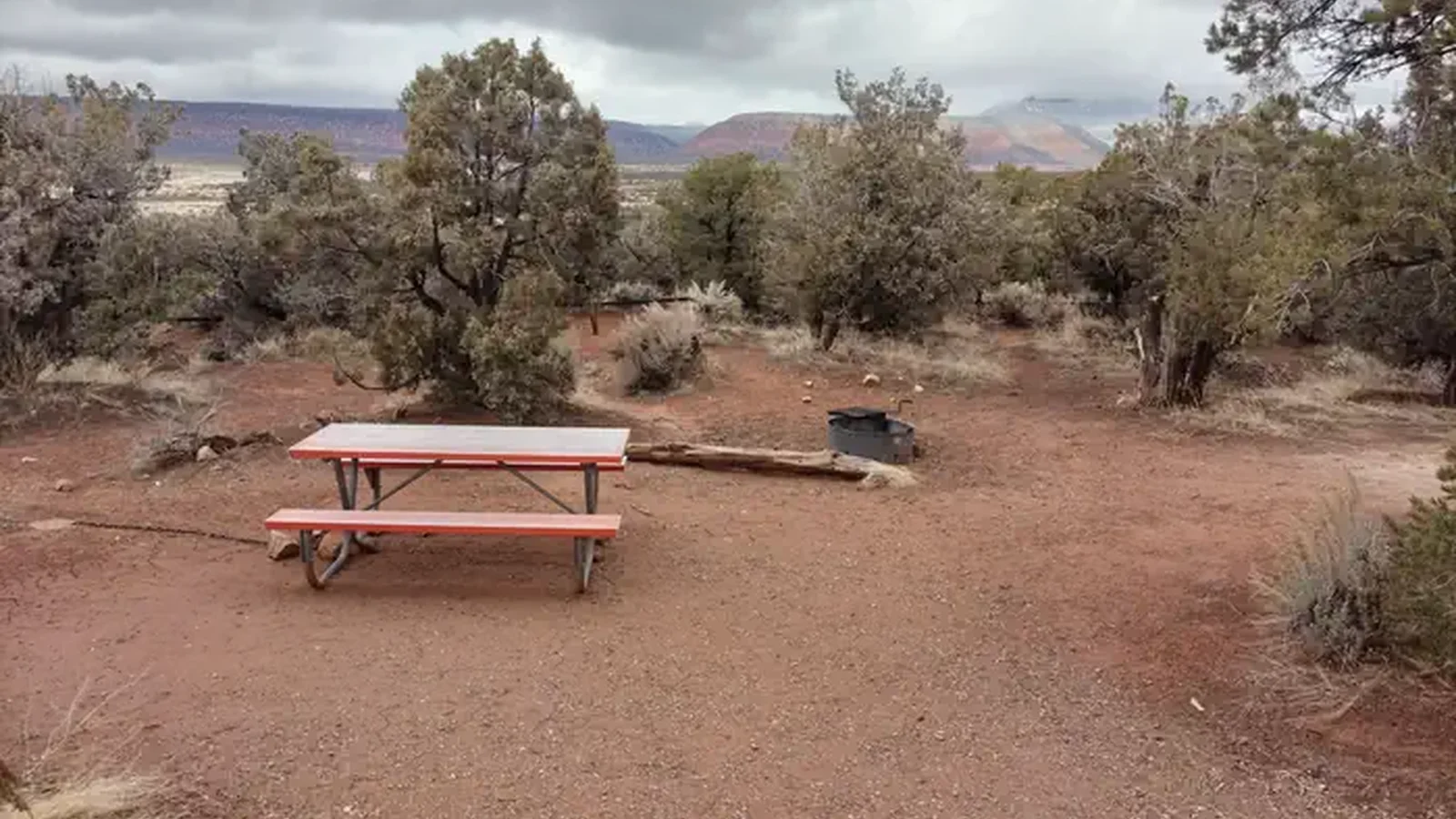 A picnic table with juniper trees in the background, under a cloudy sky