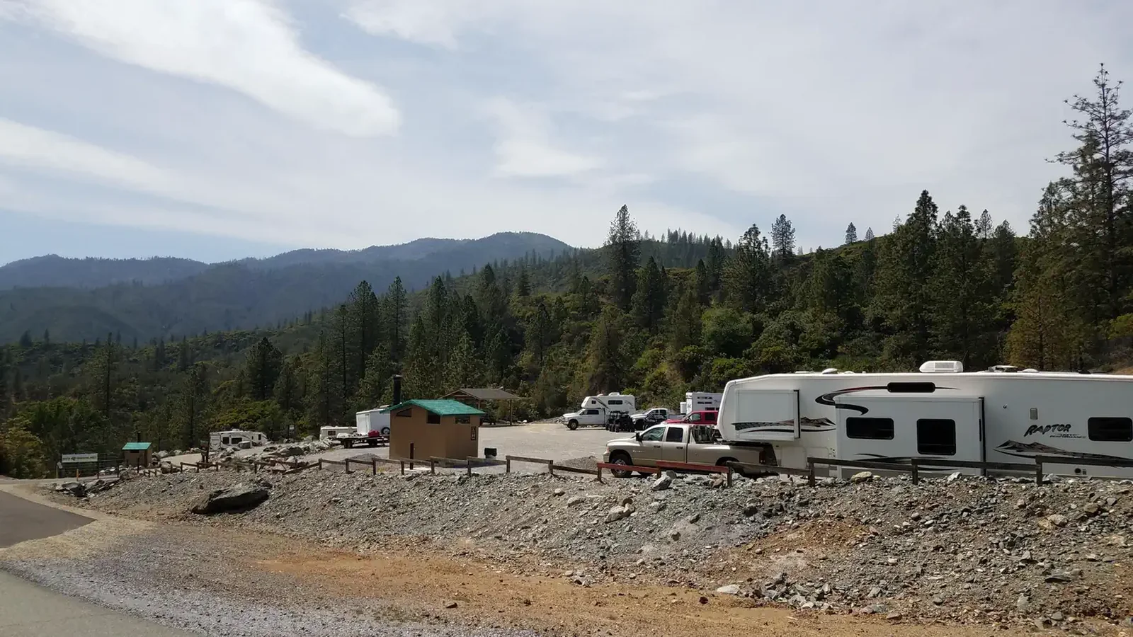 Several trucks, trailers and RVs in the camping area with treed hills in the background