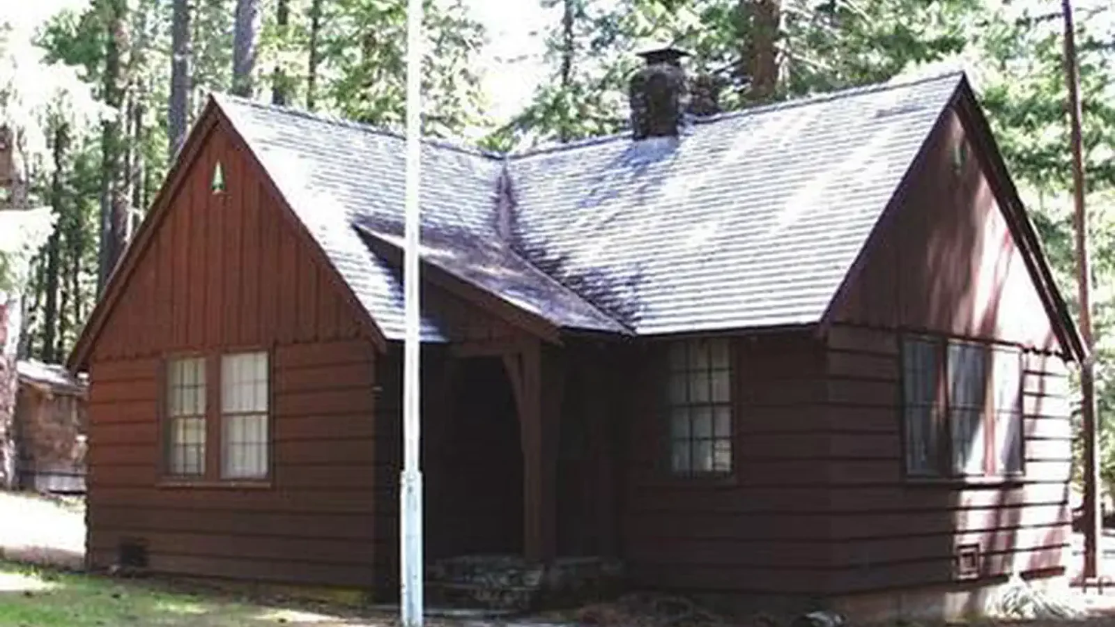 Flag pole in front of L-shaped house in conifer forest.
