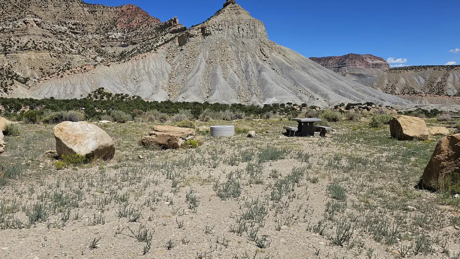 New Joe's Campground campsite. Parking area delineated with boulders. Picnic table in back of the area. Blue sky and mountains in the background.