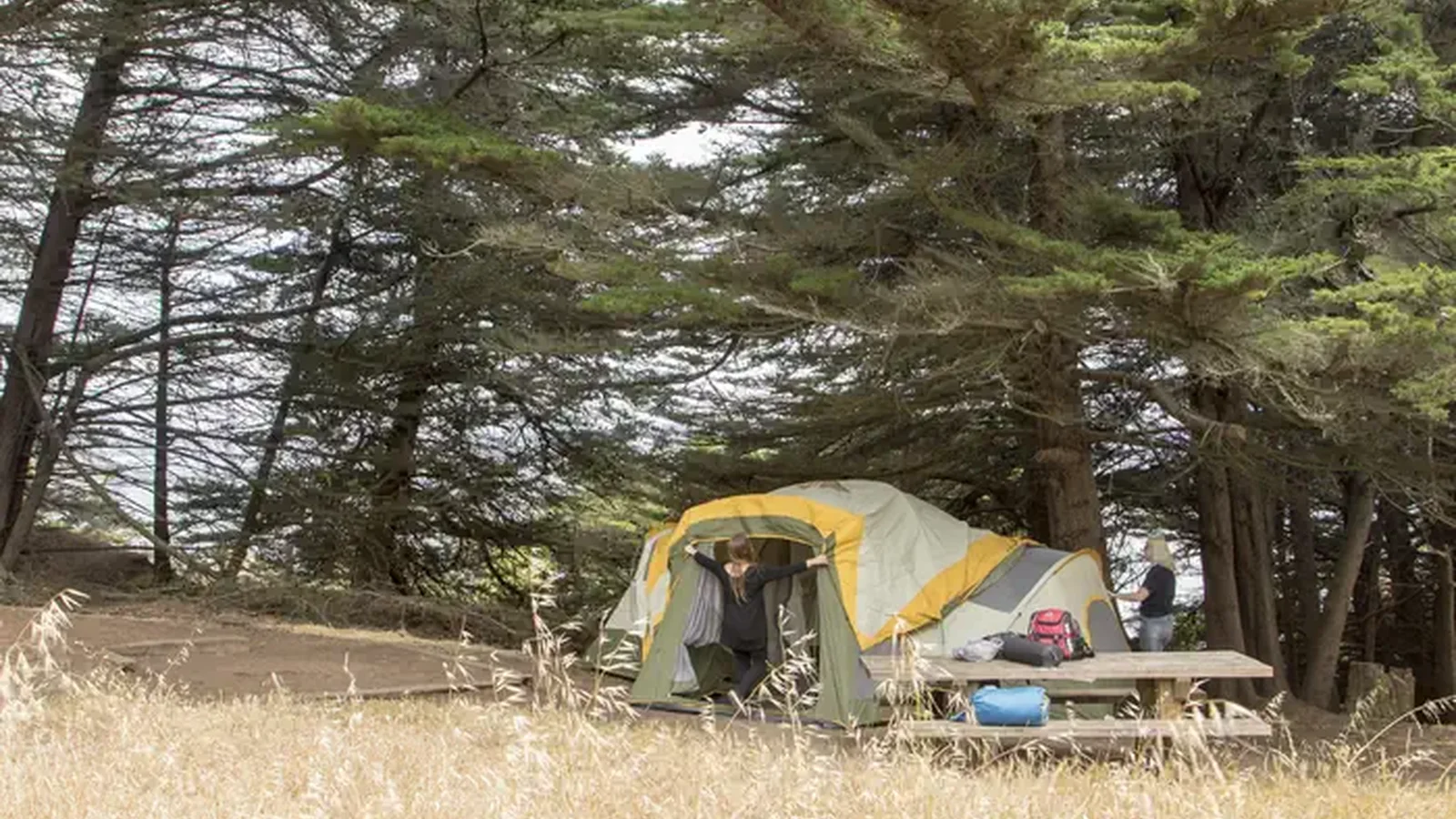 Two people set up a large tent near a picnic table at Site 3.