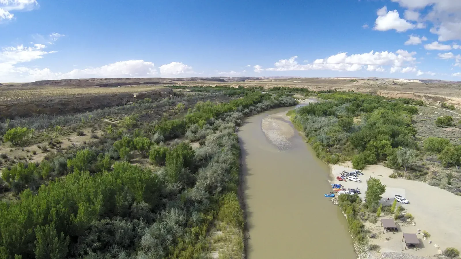 An aerial view of the San Juan River line with green cottonwood trees and the Sand Island boat launch area.