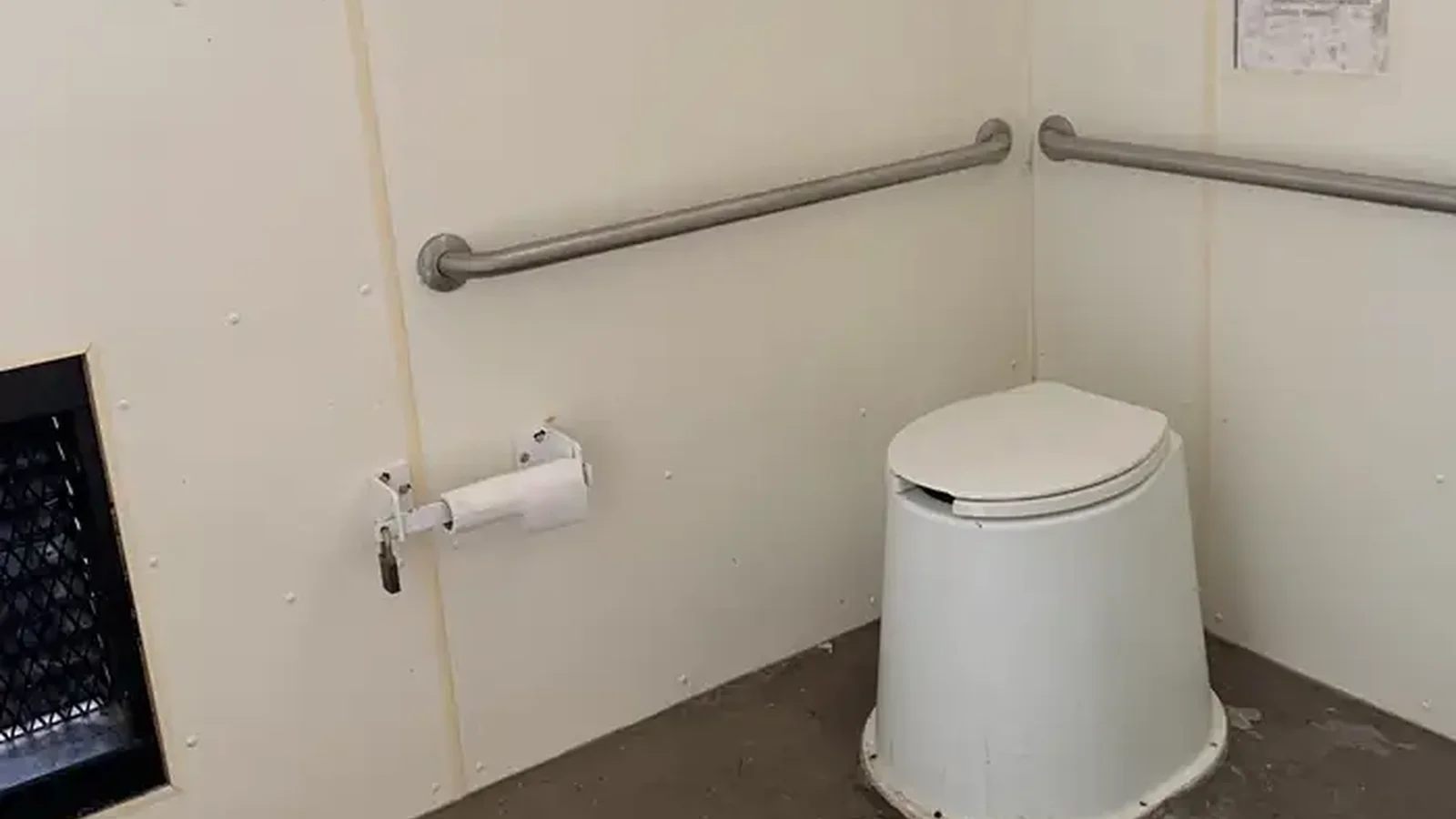 A toilet in the pit toilet building with rolls of toilet paper on the left.
