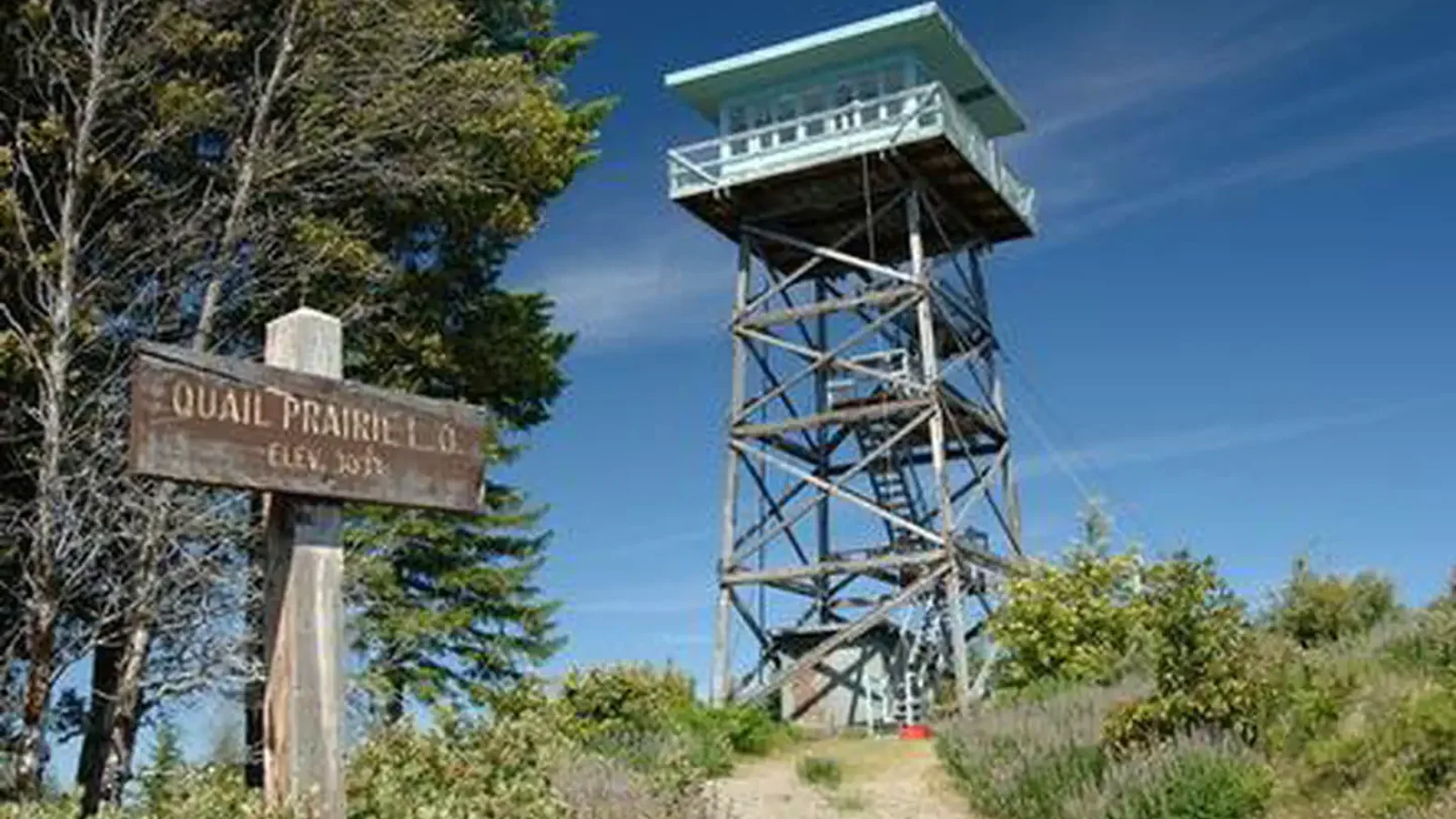 Lookout tower from below with sign in foreground and blue sky in the background.